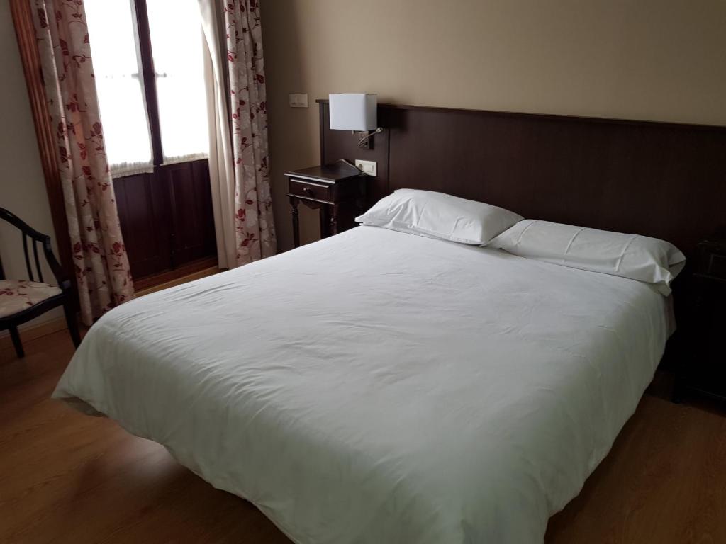1 dormitorio con 1 cama grande con sábanas y almohadas blancas en Hotel Rey Sancho IV, en Santisteban del Puerto