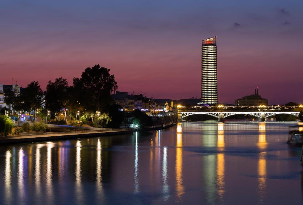 een brug over een rivier met een gebouw 's nachts bij Eurostars Torre Sevilla in Sevilla