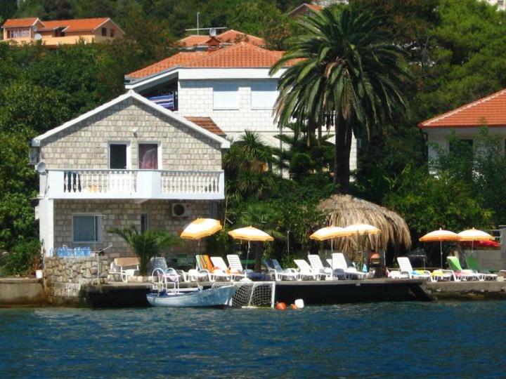 a house with a dock with chairs and umbrellas on the water at Apartments Roza in Herceg-Novi
