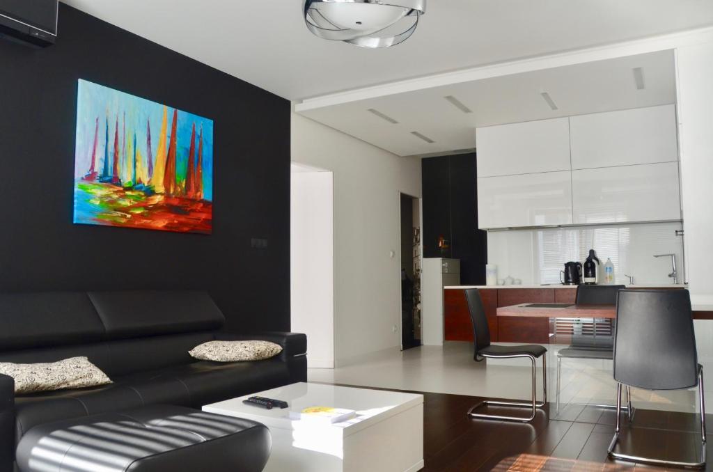 a living room with a black couch and a kitchen at Apartament Wzgórze Słowików in Warsaw