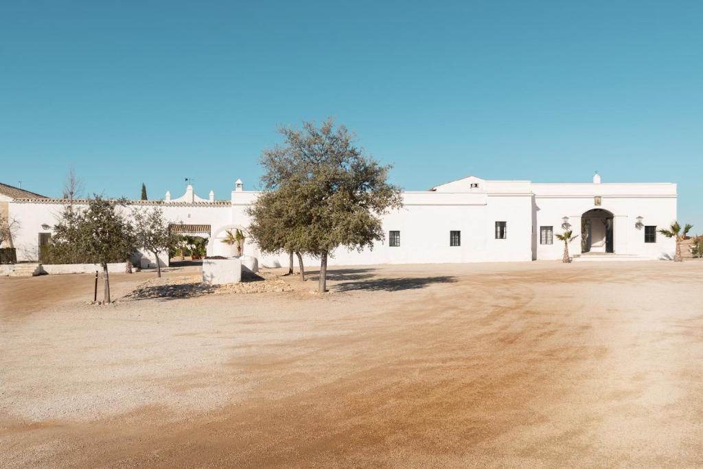 un edificio blanco con un campo de tierra delante de él en HACIENDA LAS MESAS - Luxury Villa Jerez, en Jerez de la Frontera