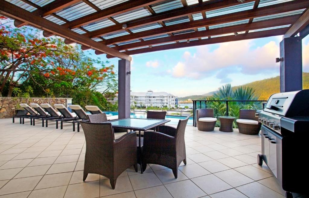 a patio with a table and chairs and a grill at at Waterfront Whitsunday Retreat - Adults Only in Airlie Beach