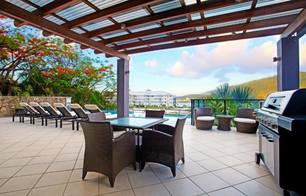 un patio con mesa, sillas y parrilla en at Waterfront Whitsunday Retreat - Adults Only, en Airlie Beach