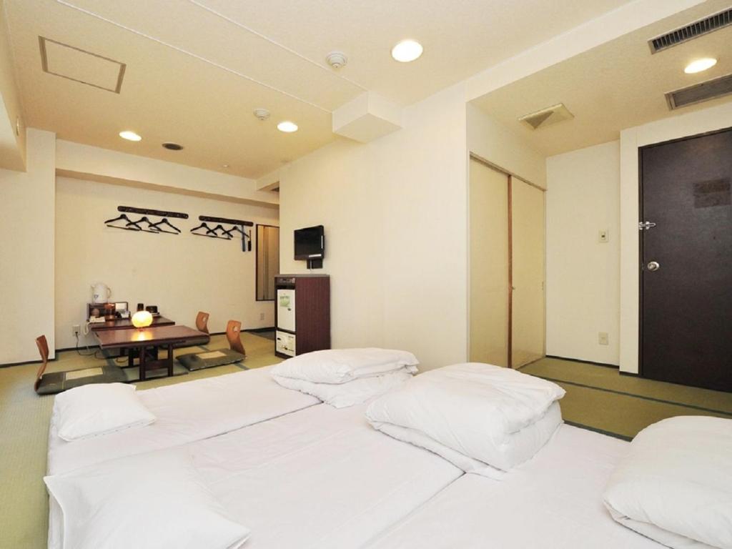 a room with four white beds and a table at Hotel Paco Obihiro Chuo in Obihiro