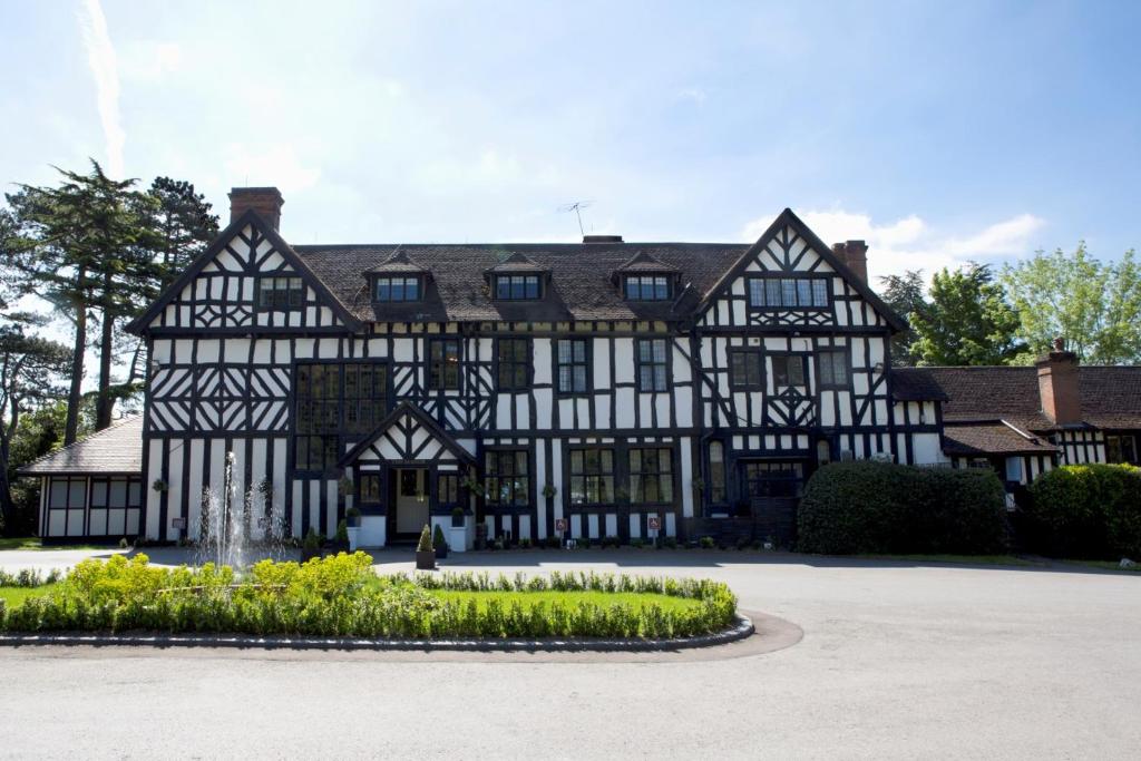 Un ancien bâtiment noir et blanc avec une fontaine dans l'établissement The Manor Elstree, à Elstree