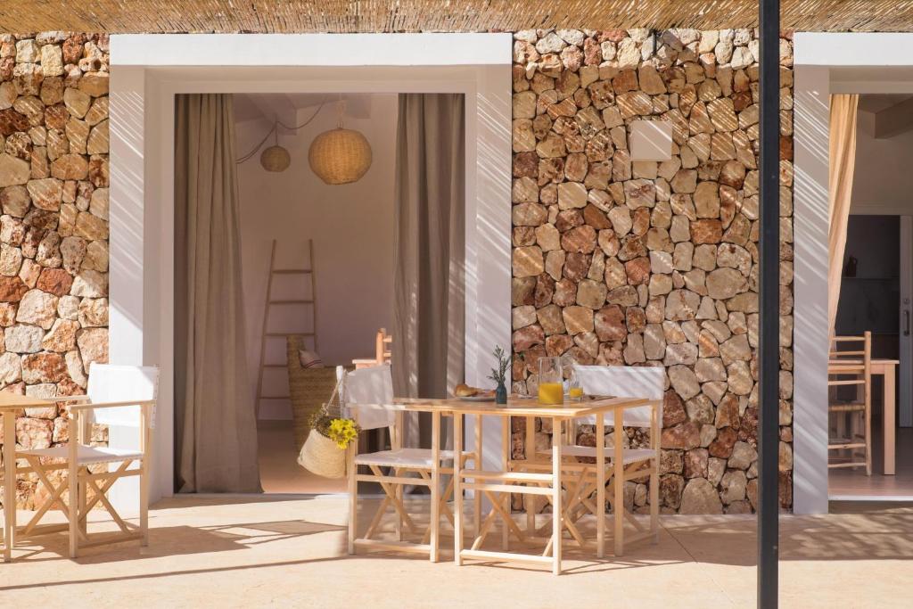 un patio con mesa, sillas y pared de piedra. en Agroturismo Ses Talaies en Ciutadella