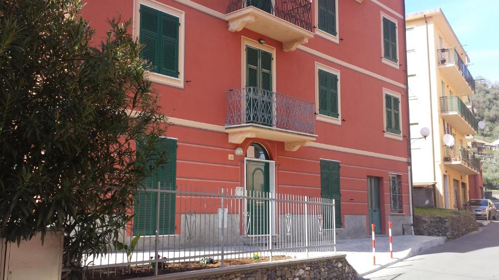 a red building with green shutters on a street at Appartamenti Enrica in Moneglia