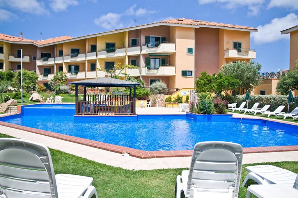a swimming pool with chairs and a building at Appartamento in complesso con piscina in Santa Teresa Gallura