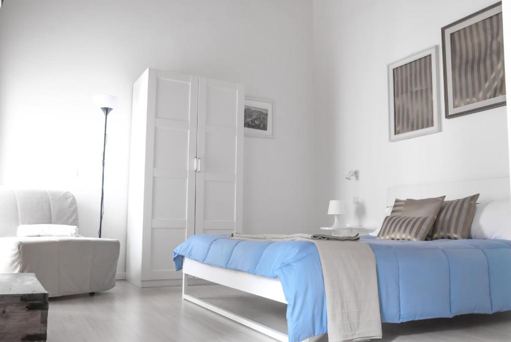 a white bedroom with a blue bed and a chair at Bookbreakfast in Terme Vigliatore