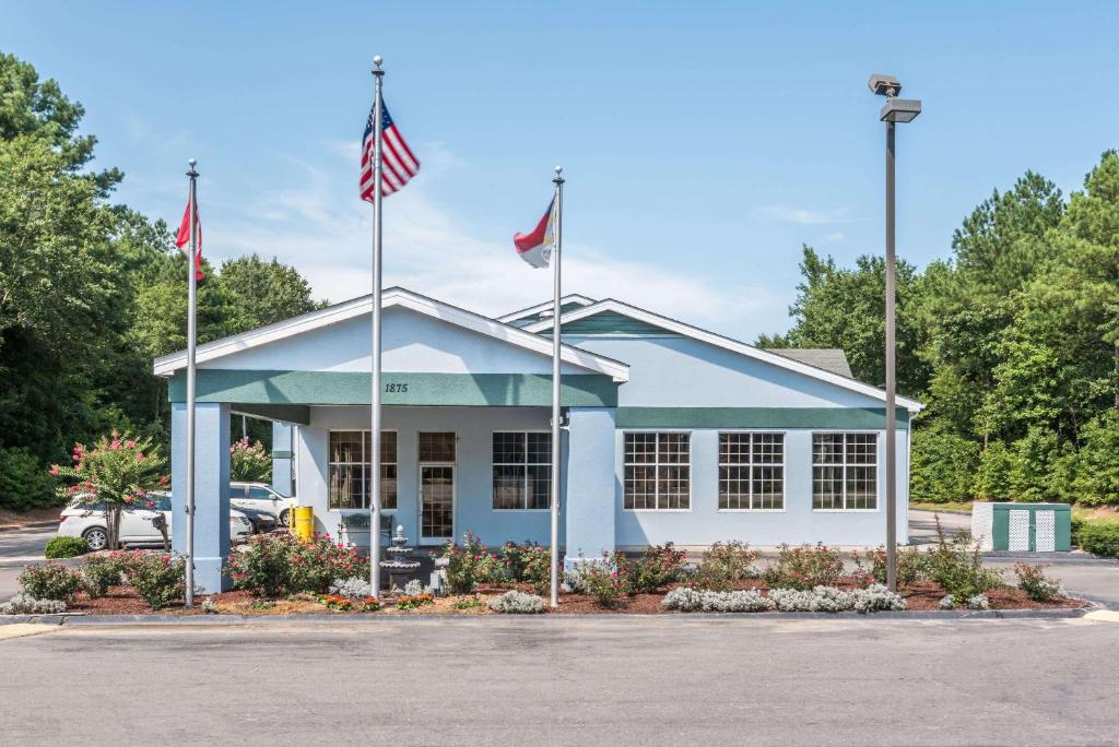 un bâtiment avec deux drapeaux dans un parking dans l'établissement Super 8 by Wyndham Fayetteville, à Fayetteville