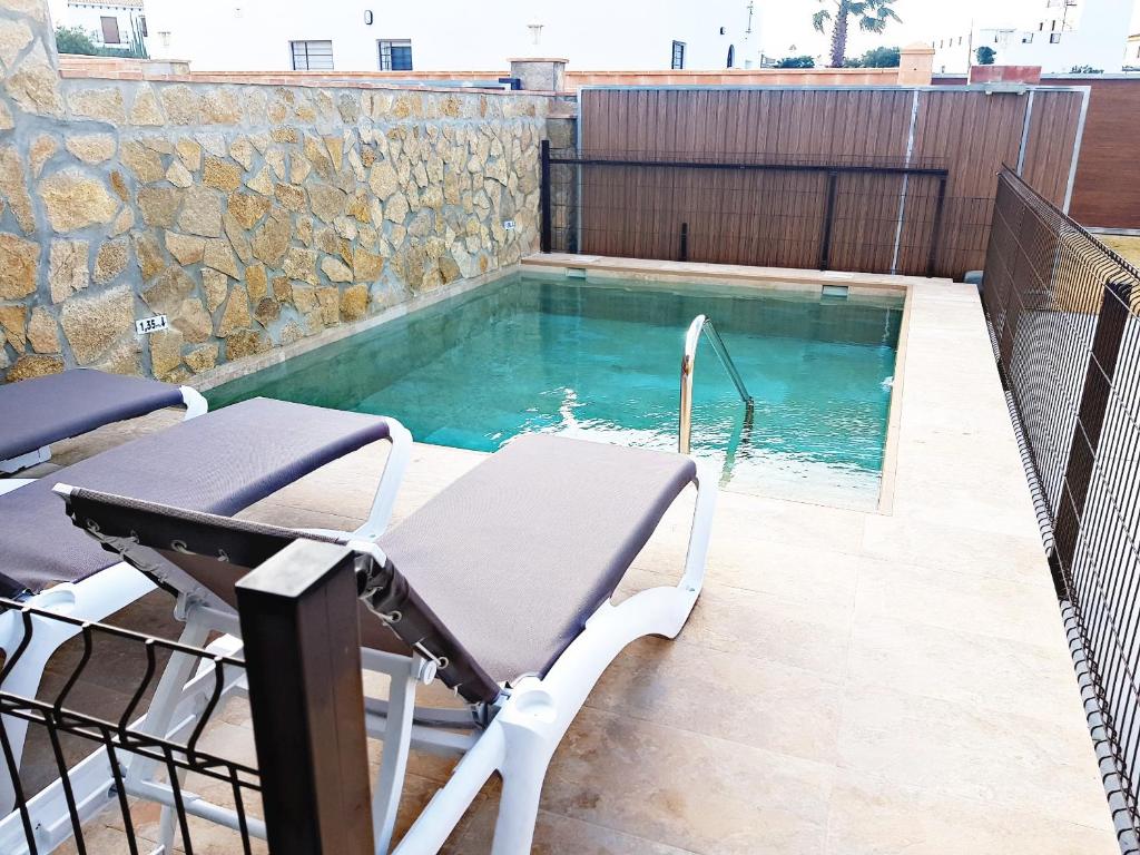 a swimming pool with two chairs and a table at Casas Miguel SOLO PARA FAMILIA in Conil de la Frontera