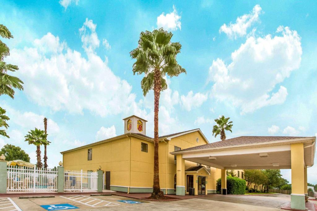 a yellow building with a clock tower and palm trees at Super 8 by Wyndham Lake Charles/Sulphur in Lake Charles