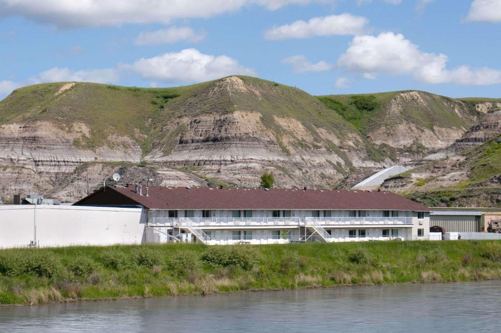 a building in front of a mountain next to a river at Travelodge by Wyndham Drumheller AB in Drumheller