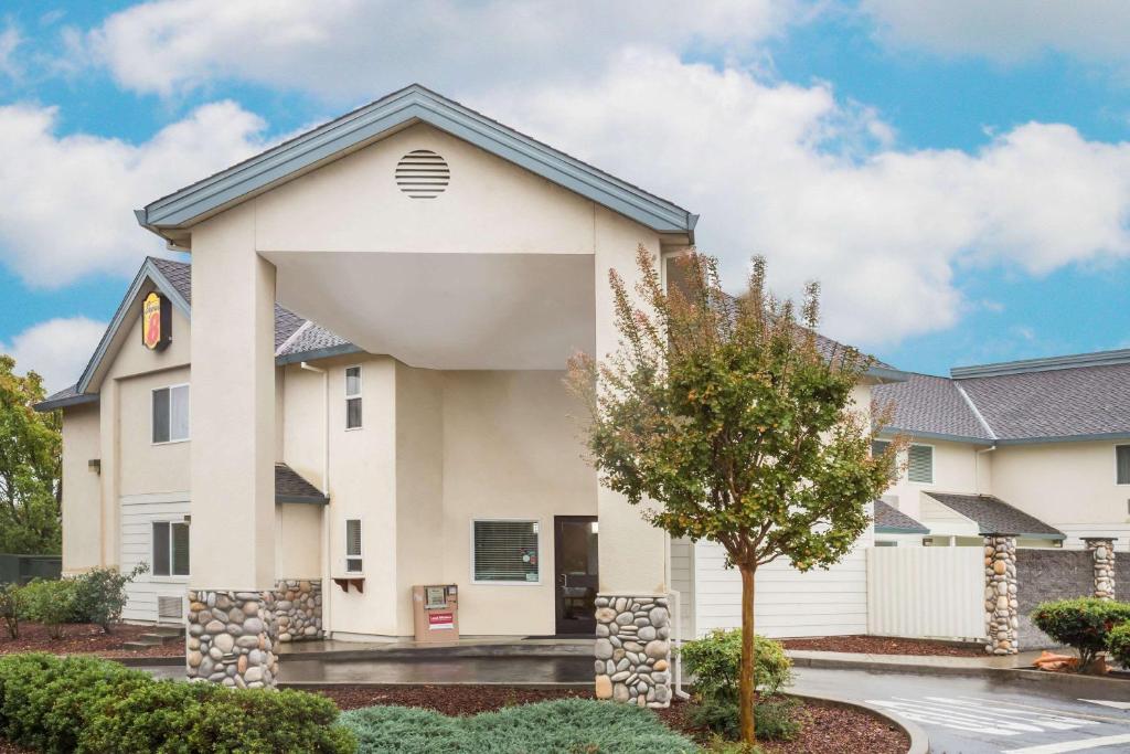 a white house with a tree in front of it at Super 8 by Wyndham Cloverdale Wine Country in Cloverdale