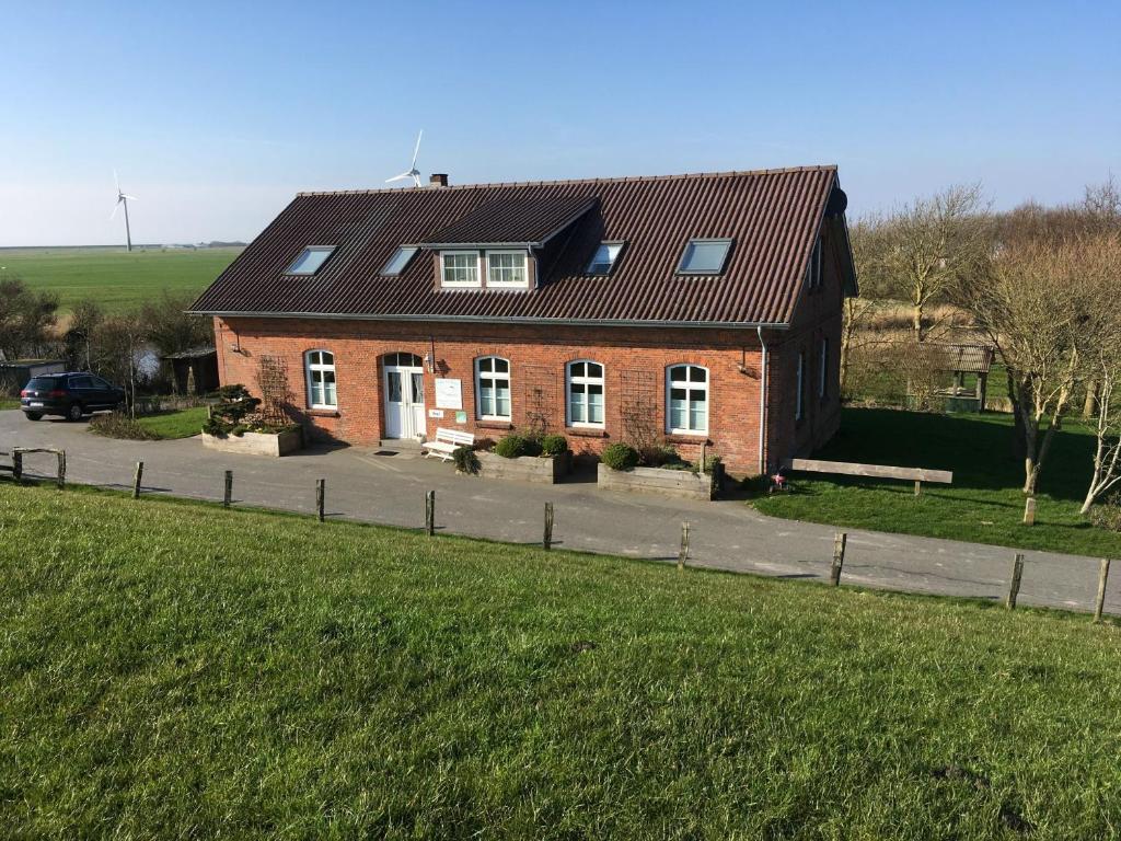 una casa de ladrillo rojo con un campo verde delante de ella en Ferienhaus Hemenswarft direkt an der Nordsee mit Meerblick en Emmelsbüll-Horsbüll