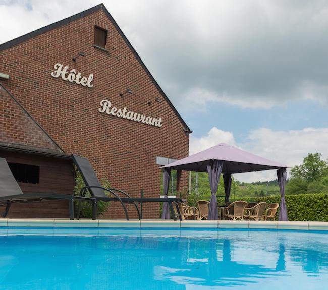 einem Pool mit Stühlen und einem Sonnenschirm neben einem Gebäude in der Unterkunft Auberge de la Lesse in Celles