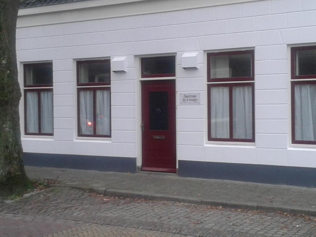 a white building with a red door and windows at Searose B@B in Serooskerke