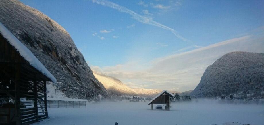 a snow covered area with a building and mountains at Vihar apartmaji in Bohinj