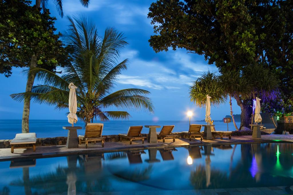 ein Pool mit Stühlen und das Meer in der Nacht in der Unterkunft Pondok Pitaya Balian Hotel in Selemadeg