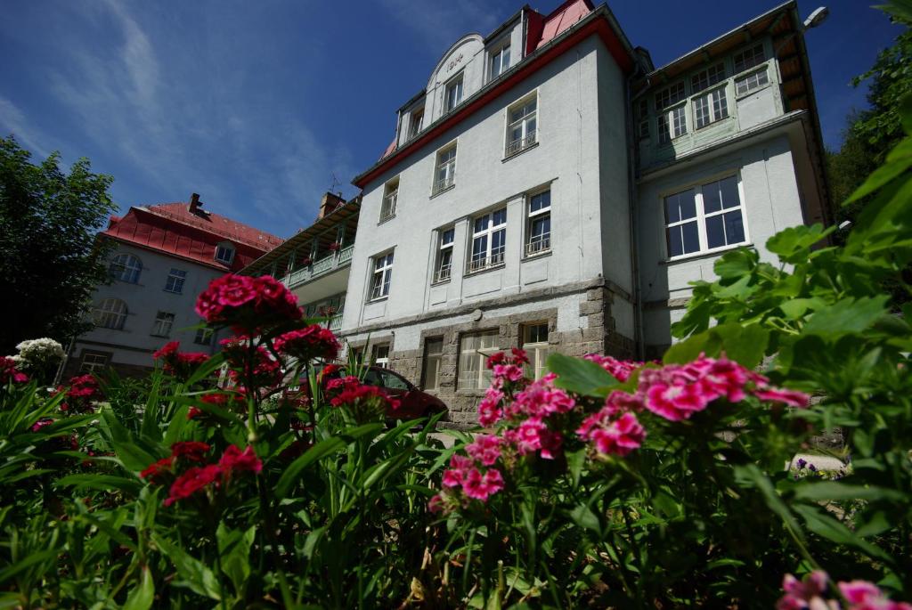 a white building with pink flowers in front of it at Ośrodek Wypoczynkowy Rzemieślnik in Szklarska Poręba