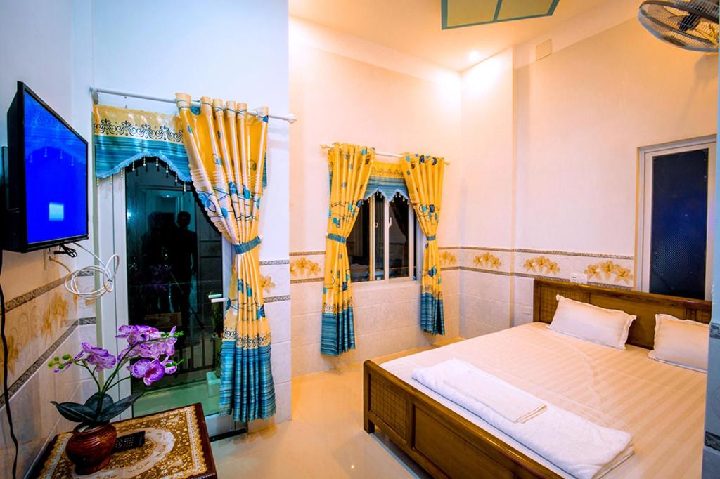a bedroom with a bed with yellow curtains and a tv at Motel Thuyền & Biển in Ly Son