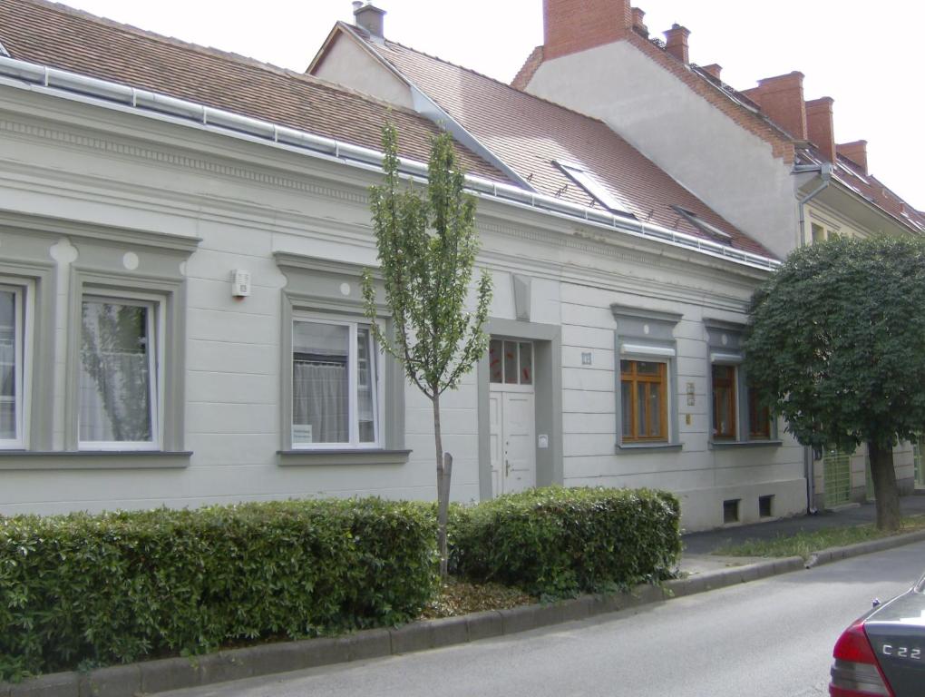 ein weißes Haus mit einem Baum davor in der Unterkunft Csapd le Csacsi Vendégház in Pécs