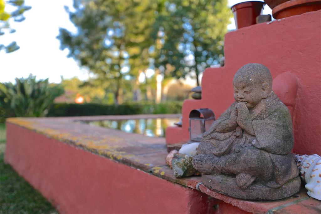 una piccola statua di un bambino seduta su un muro rosso di Monte da Xica - Somente Adultos a Zambujeira do Mar