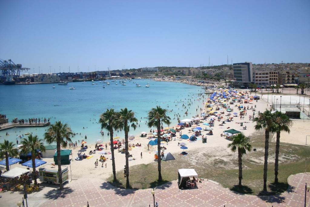 a crowd of people on a beach with palm trees at Pretty Bay Apartments in Birżebbuġa