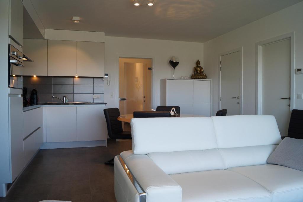 a living room with a white couch and a kitchen at Villa Jalina Sailors Beach in Nieuwpoort