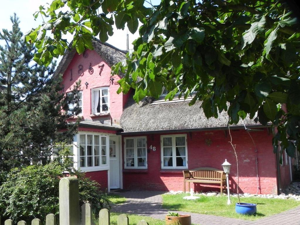 a red house with a bench in front of it at Hüs Sanskiin Ferienwohnung *Goodshenk* in Süddorf