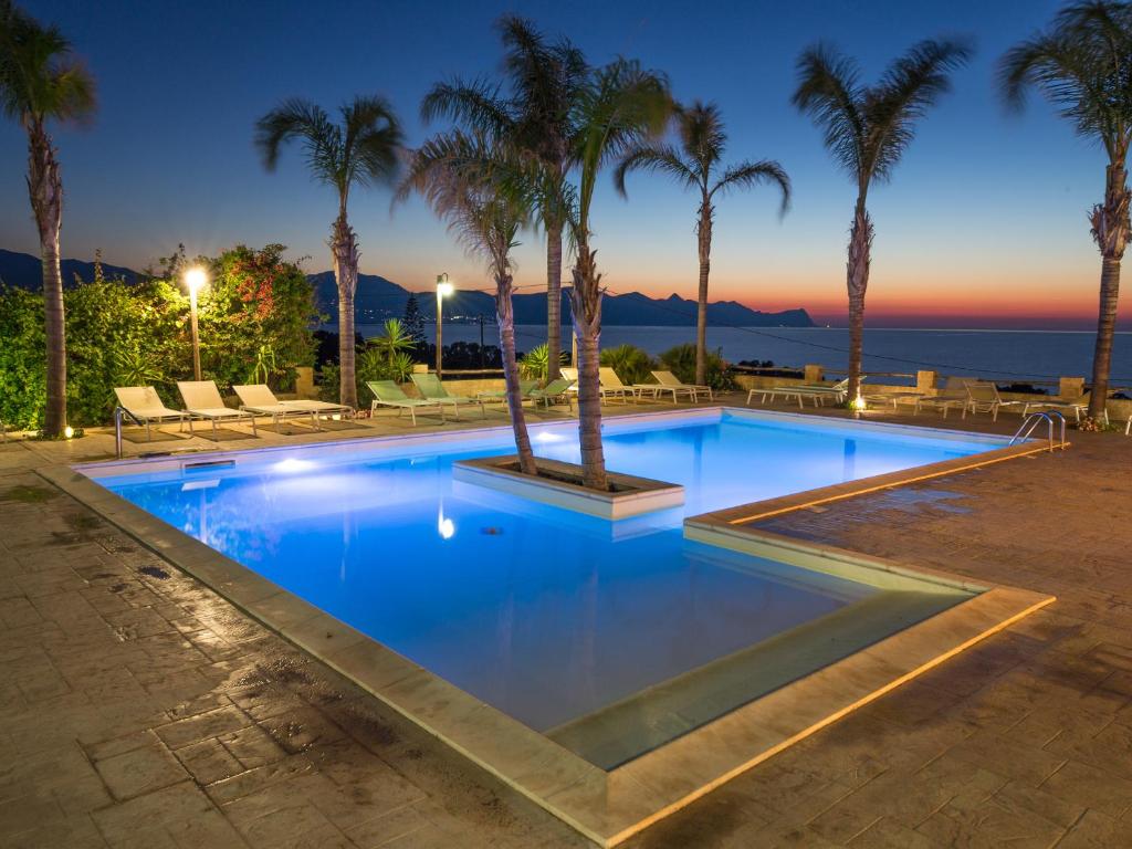 a swimming pool with palm trees and the ocean at Petruso Resort in Balestrate
