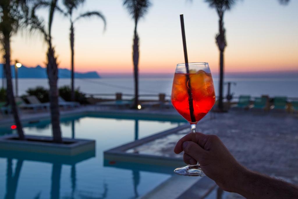 a person holding a drink in front of a pool at Petruso Resort in Balestrate