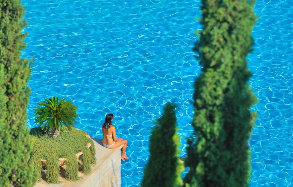 a woman sitting on the edge of a swimming pool at Anassa in Polis Chrysochous