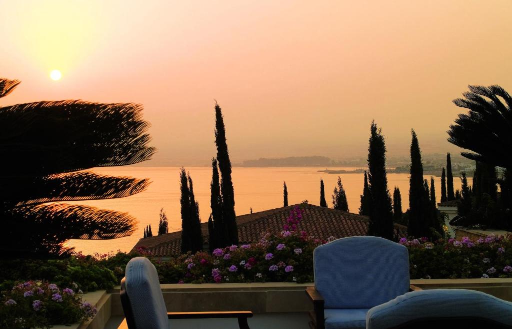 a sunset over the water with two chairs and trees at Anassa in Polis Chrysochous