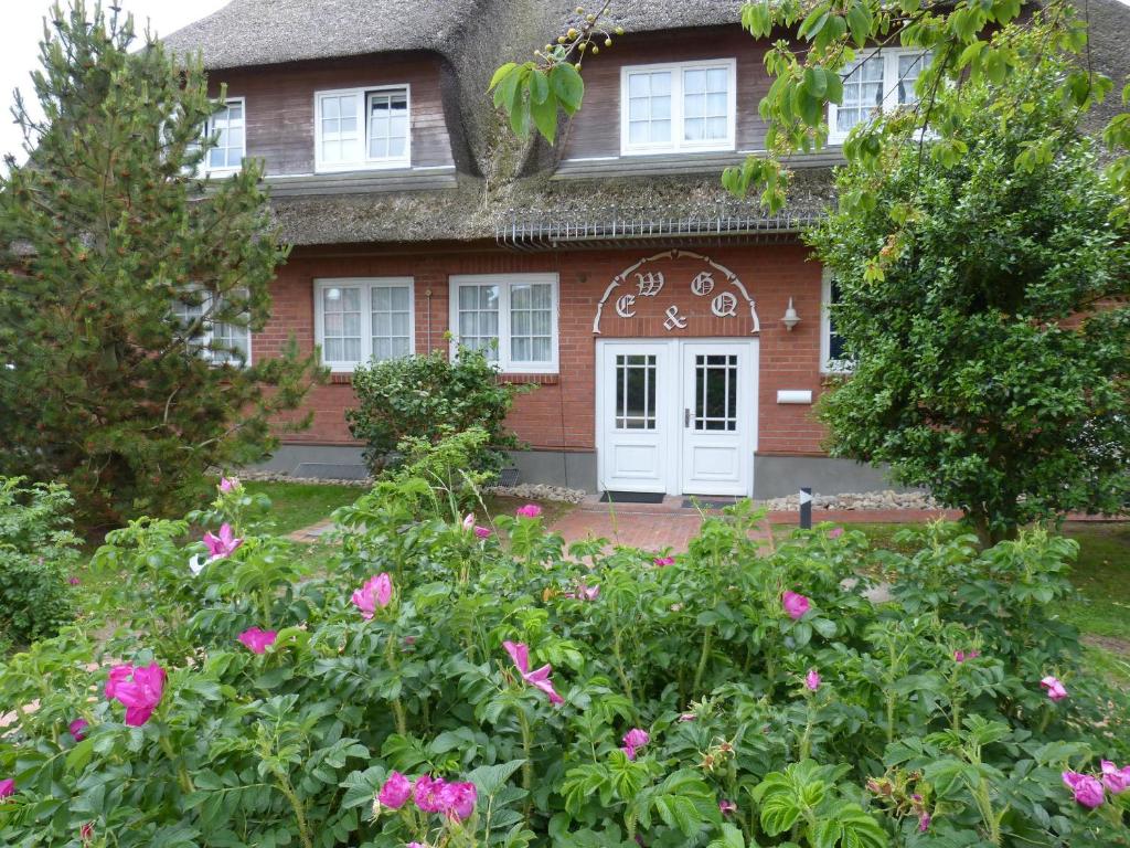 ノルドドルフにあるFerienwohnung *Reetblick*の白い扉とピンクの花が咲く赤レンガ造りの家
