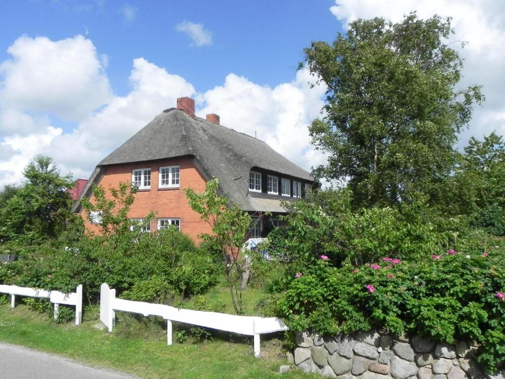 ein Haus mit einem Strohdach und einem weißen Zaun in der Unterkunft Ferienwohnung *Reethuk* in Norddorf