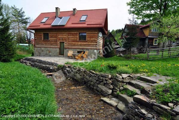 a wooden house with a red roof and a stone wall at Domek u Emilki in Korbielów