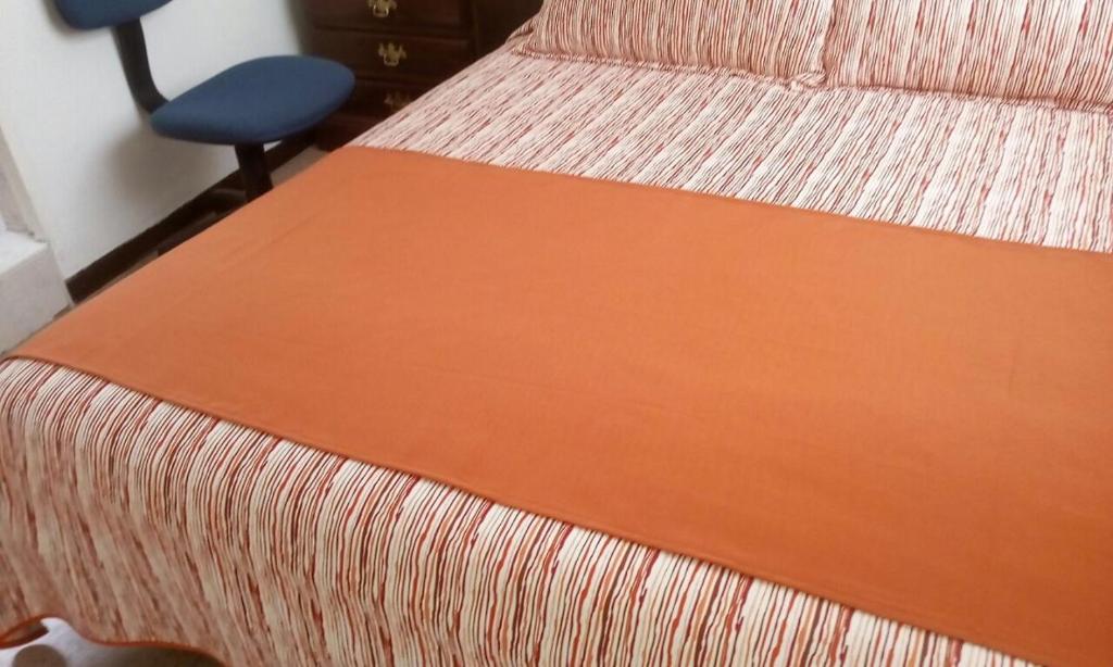 a bed with a orange blanket on it with a chair at GHL casa hotel in Bogotá