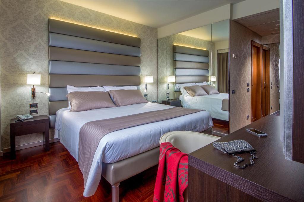 ein Hotelzimmer mit 2 Betten, einem Schreibtisch und einem Spiegel in der Unterkunft Enea Hotel Pomezia in Pomezia