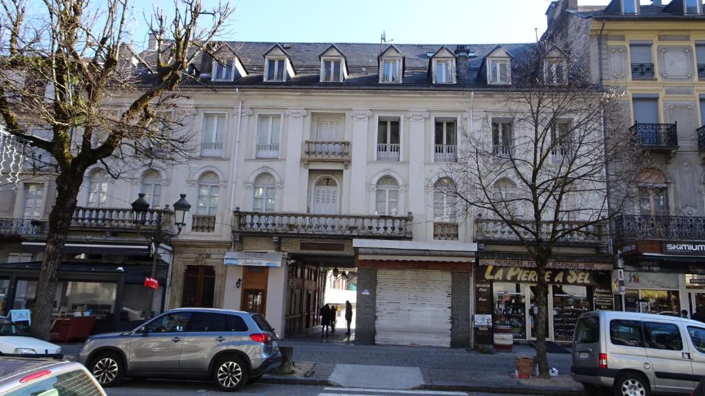 een groot wit gebouw met auto's ervoor geparkeerd bij Appart T4 Luchon plein centre in Luchon