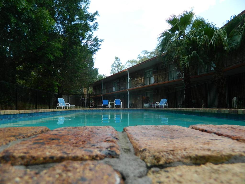 a swimming pool with chairs and a building at Coomera Motor Inn in Gold Coast