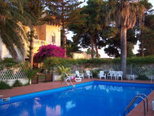 a swimming pool with chairs and palm trees and a house at B&B Villa Amodeo in Paceco