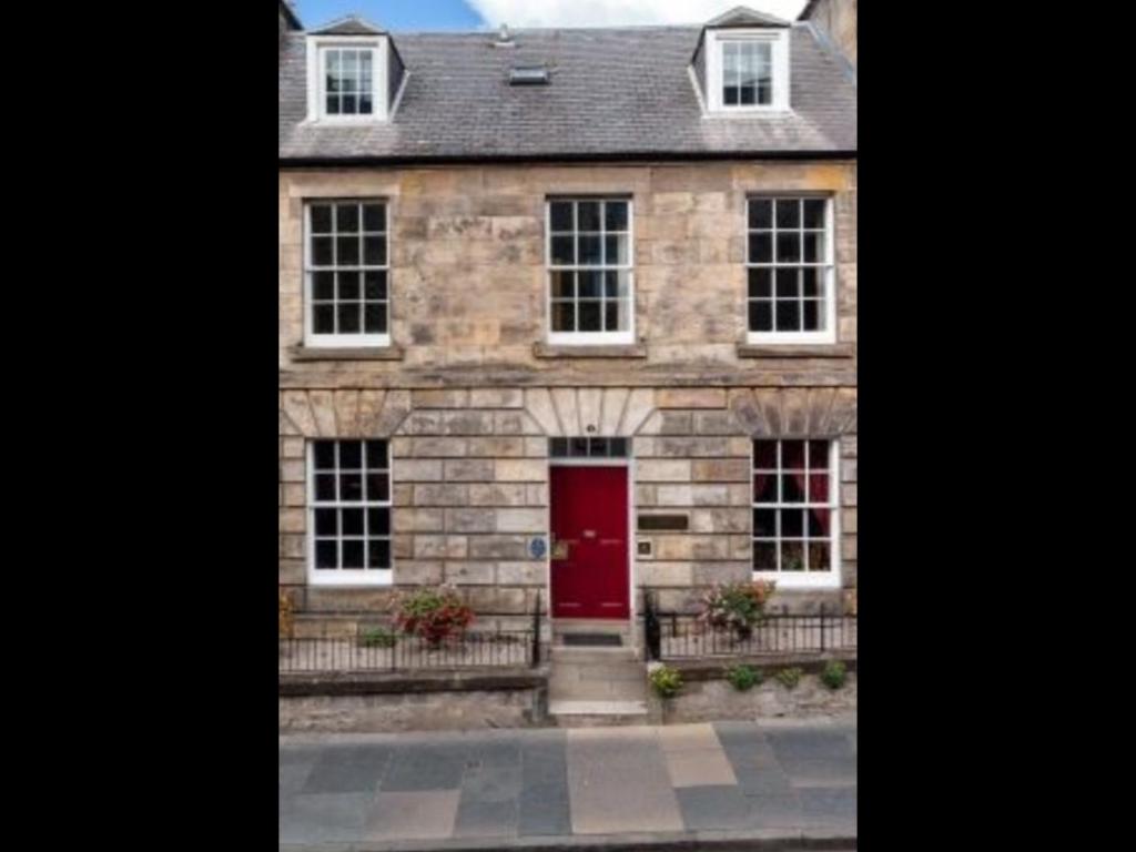 uma casa de pedra com uma porta vermelha numa rua em No 5 Pilmour em St. Andrews