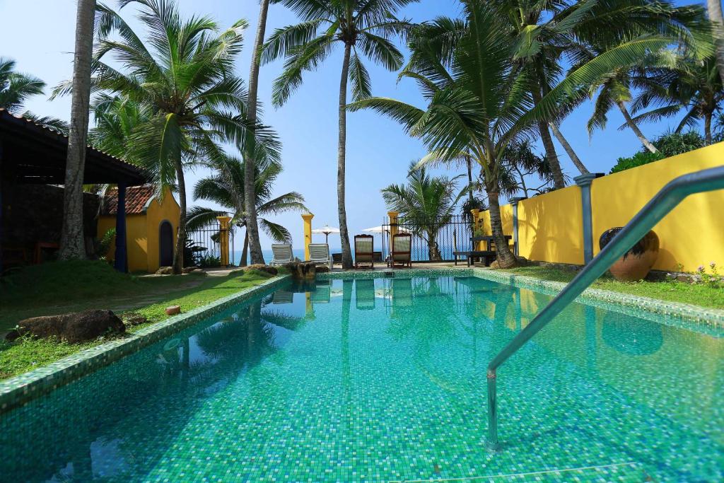a swimming pool with palm trees in the background at Villa Kusum in Hikkaduwa