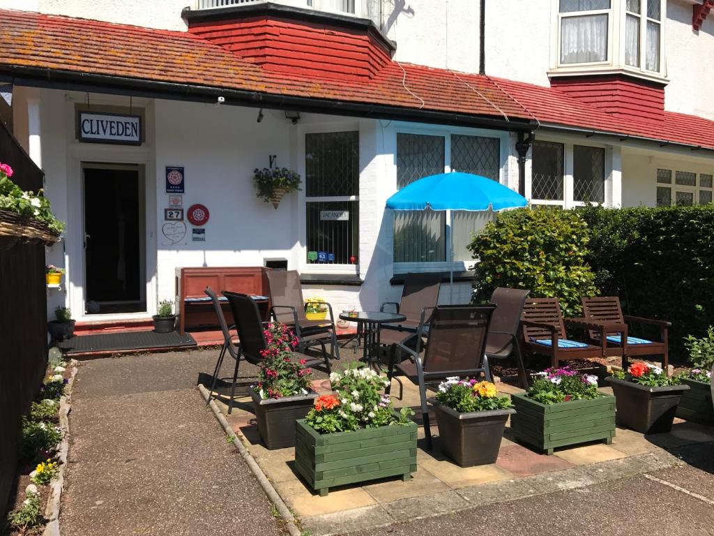 un patio con sillas, sombrilla y flores en Cliveden Guest House, en Paignton