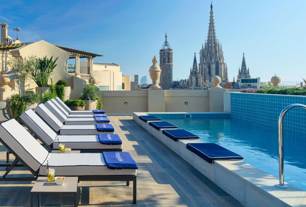 una piscina con sedie a sdraio blu e bianche accanto a un edificio di H10 Madison 4* Sup a Barcellona