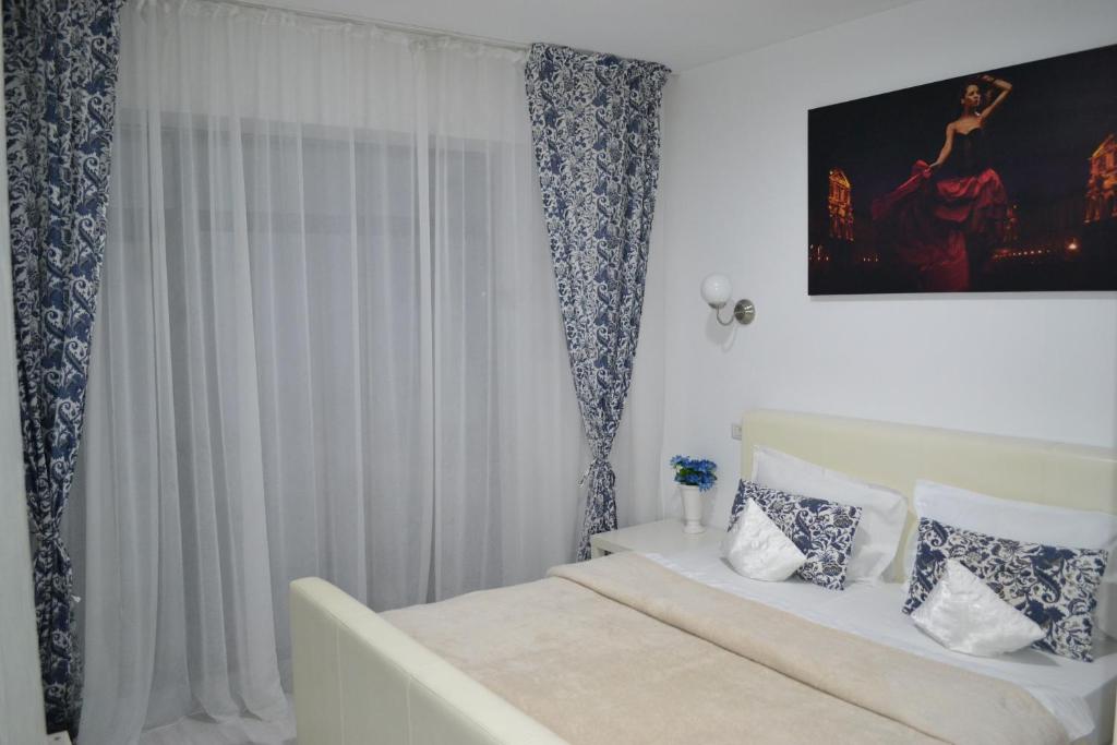 a white bedroom with a bed and a painting on the wall at City Park Residence in Constanţa