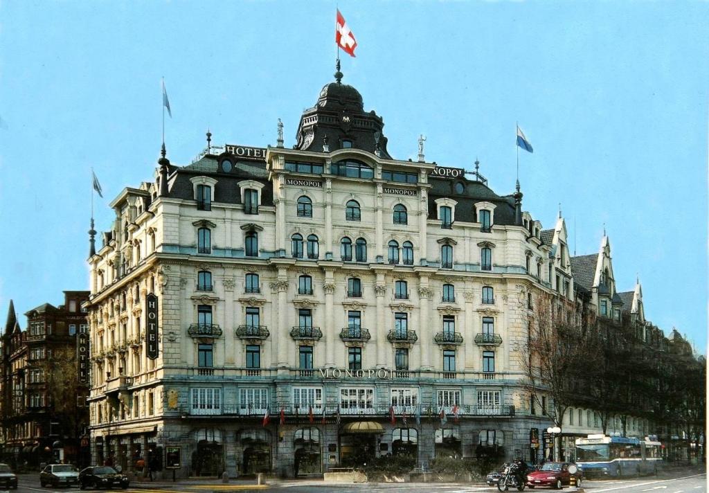 ein großes weißes Gebäude mit Flaggen darüber in der Unterkunft Hotel Monopol Luzern in Luzern