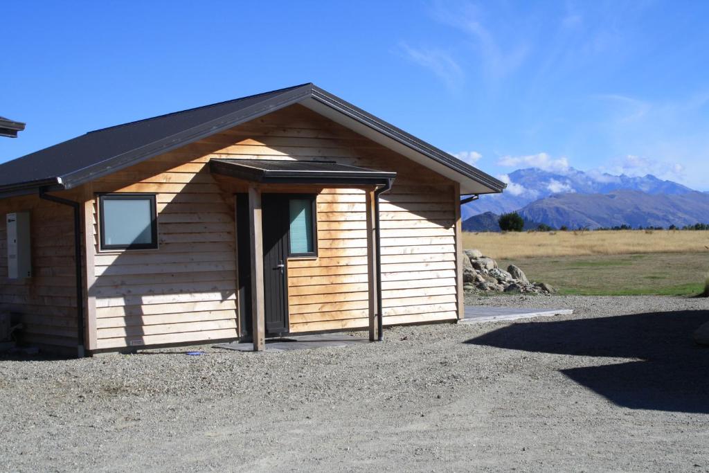 a small wooden building with a door and mountains in the background at Mt Barker in Wanaka
