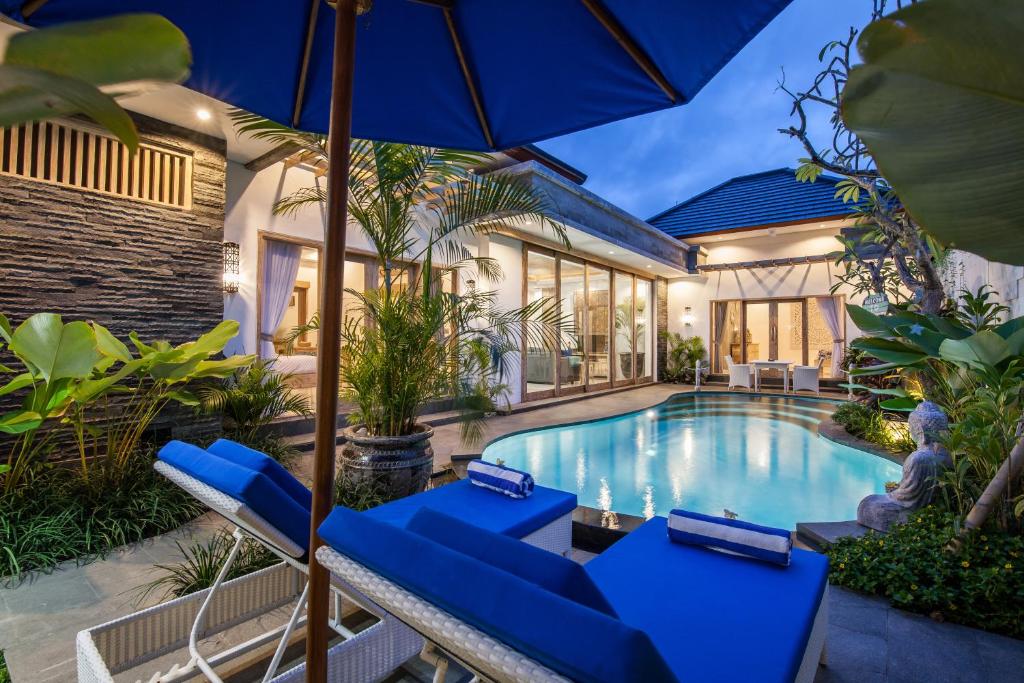 een zwembad met blauwe stoelen en een parasol bij Ambermoon Villa 2 in Seminyak